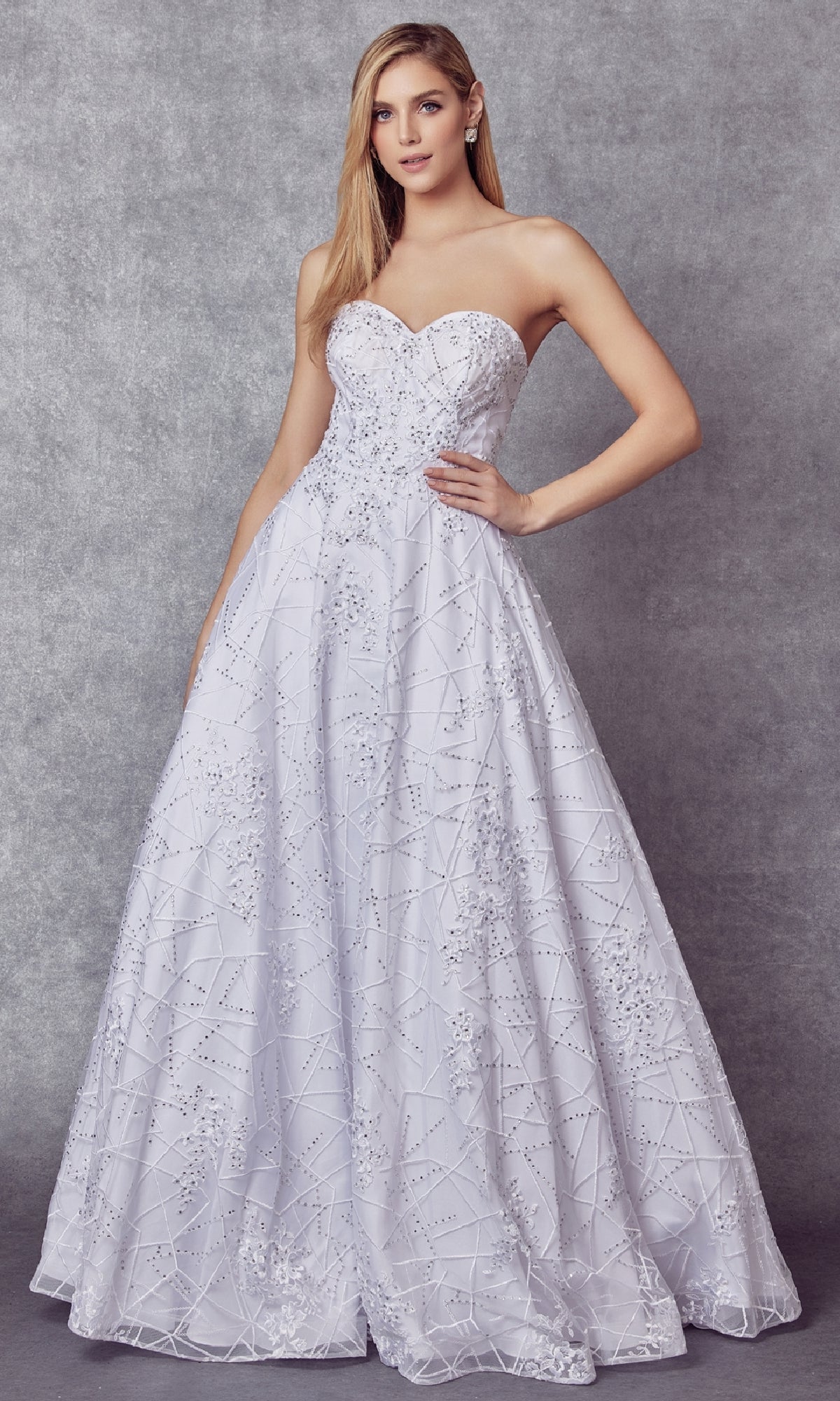 A woman in the Juliet 692 long prom dress, featuring a strapless sweetheart neckline and sequin-detailed fitted bodice, stands against a gray textured background.